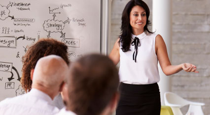 dark haired woman speaking to a meeting room